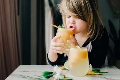 Girl sipping a glass of sparkly mango slushy about to spill