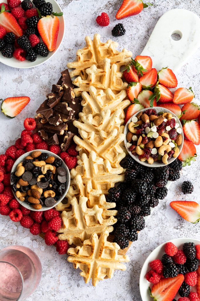 Brunch board for Mother's Day with waffles, fruits like raspberries and strawberries and blackberries, cashews, and chocolate.